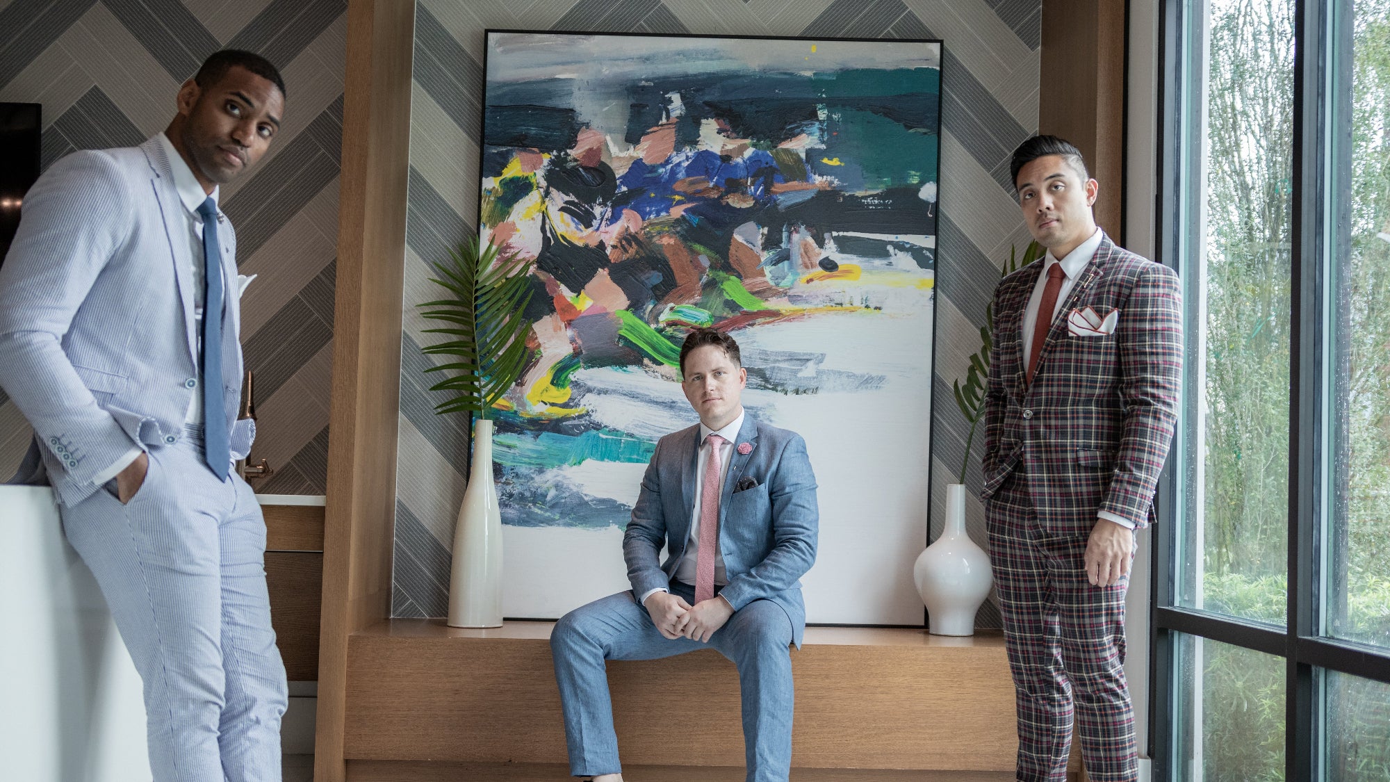 Three men wearing suit and tie in front of a large geometric artwork piece
