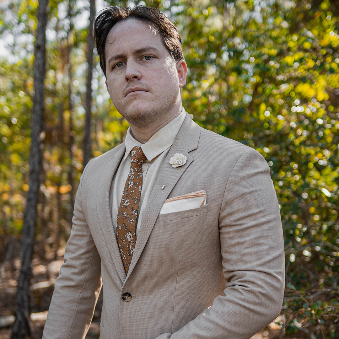 Man wearing a khaki suit and floral brown wedding tie in a wooded area