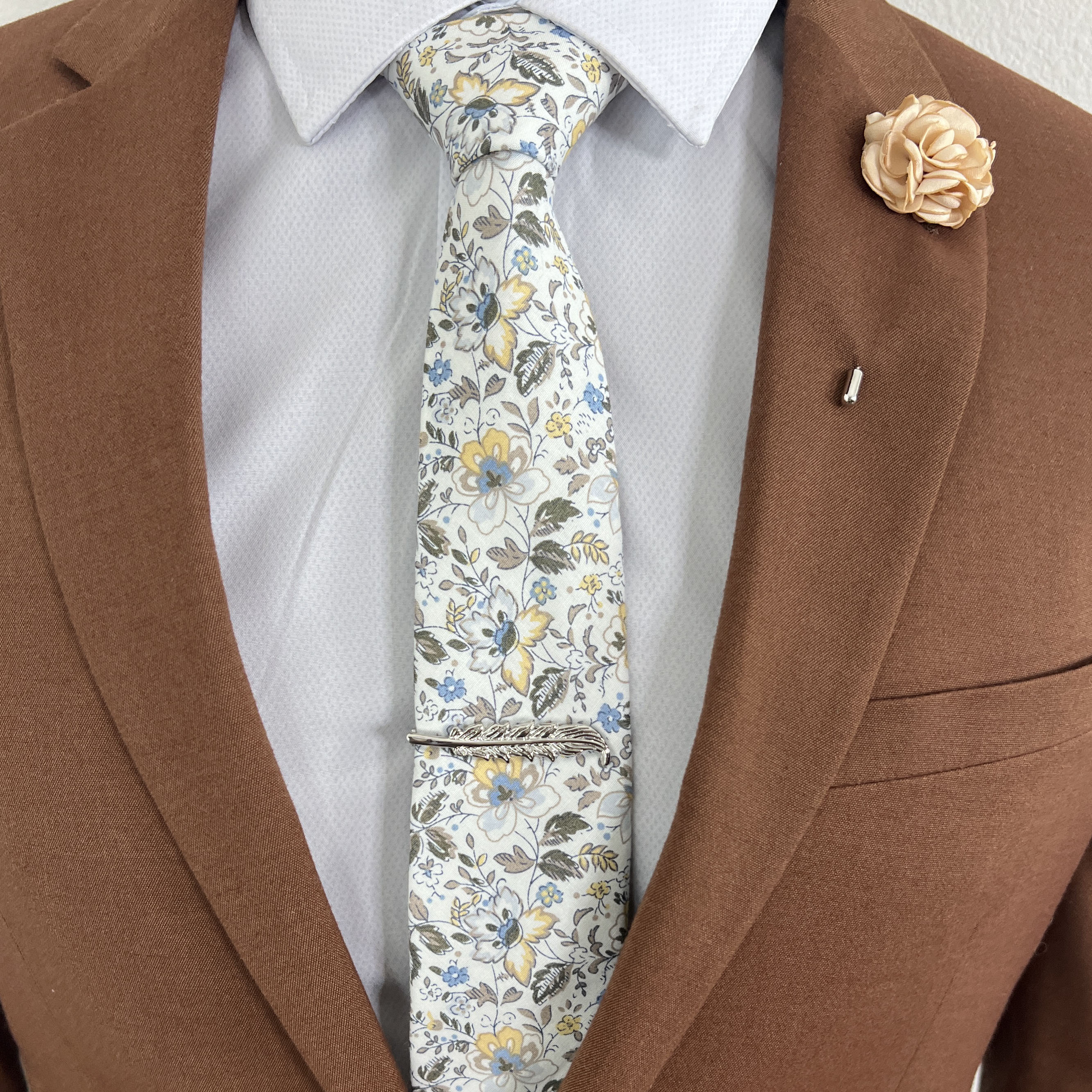 Silver Feather tie bar on a white floral tie and a brown suit