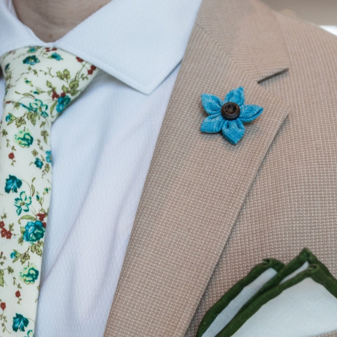Wildflower linen light blue lapel pin over a tan suit lapel.
