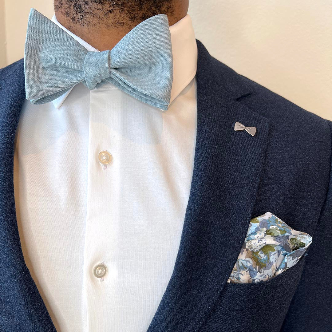 Man wearing a navy blazer with a light blue bow tie and floral pocket square.