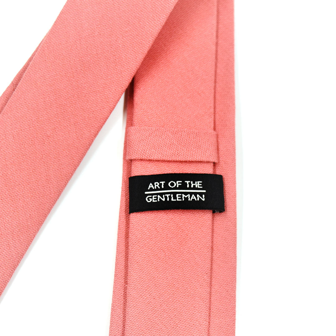 Coral pink tie with a label reading 'Art of the Gentleman' on a white background