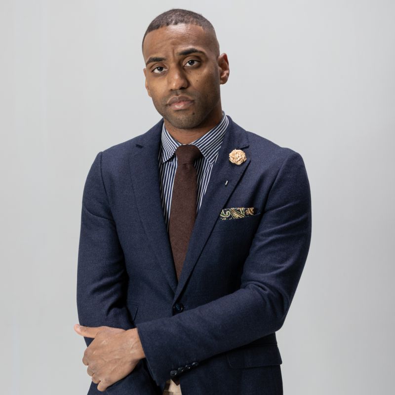 Man wearing a navy suit with a brown tie and floral pocket square on a light gray background
