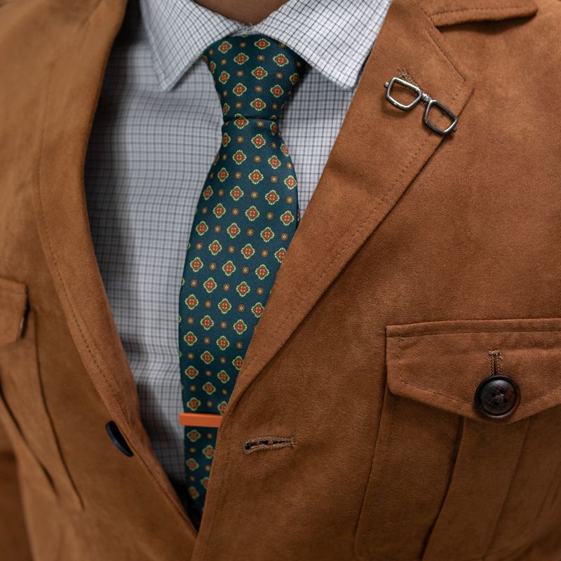 Brown suit jacket with a patterned tie and glasses holder on a light blue shirt.