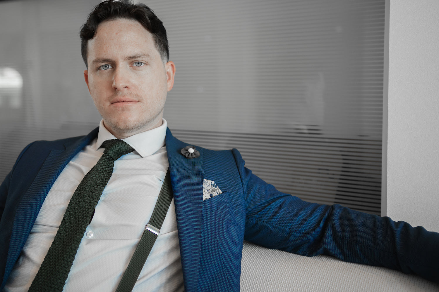 A man wearing a blue suit with olive green suspenders and tie