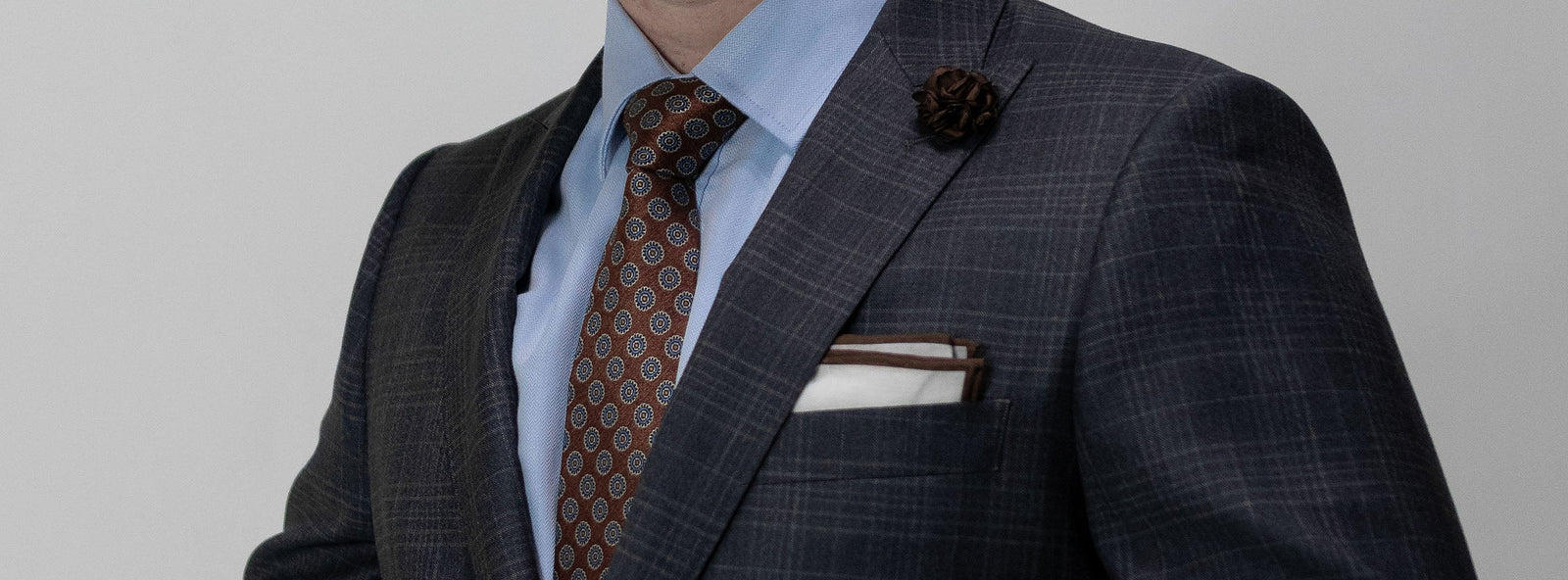 Man wearing a blue dress shirt with complementary brown and blue polka dot tie and grey suit