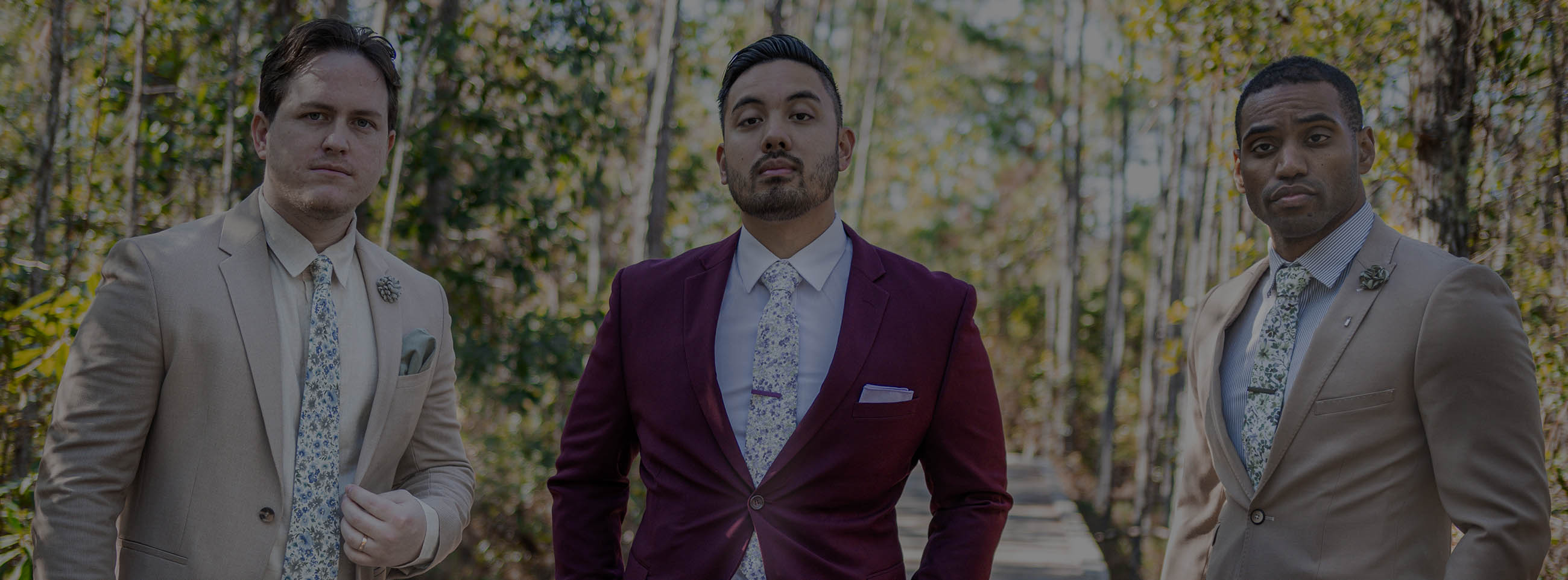 Three men standing in the woods wearing suits and floral ties. 
