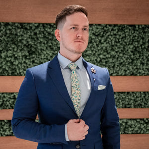 Man wearing Floral Aqua Sea Blossoms Tie with a Blue suit and a pale blue shirt in front of a foliage wall