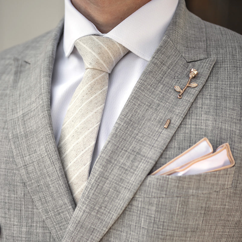Man wearing a grey suit with a champagnes tie and tan border pocket square