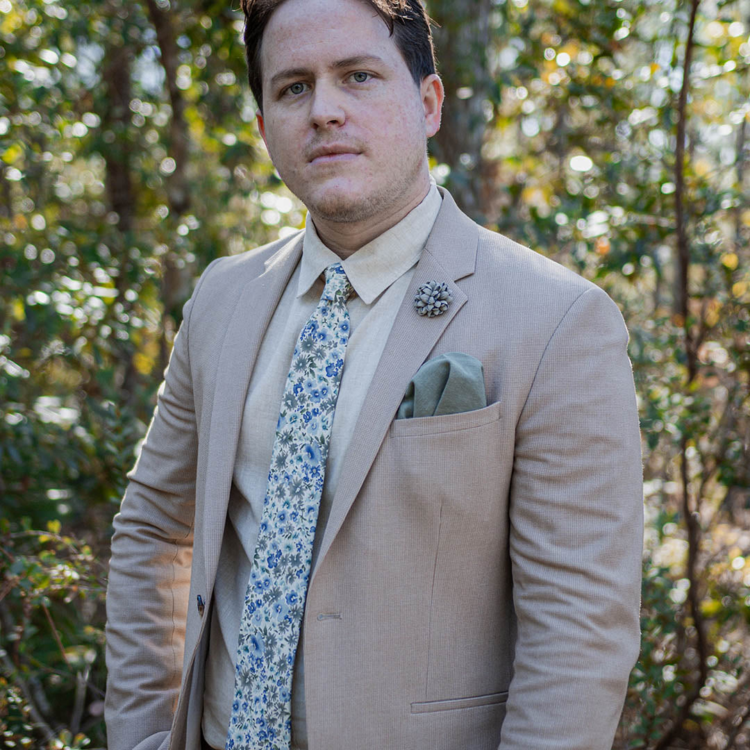 Man wearing a tan suit with a floral wedding tie in a wooded area