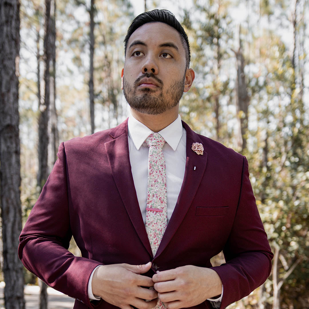 Man wearing maroon wedding suit with a light floral wedding tie in the woods