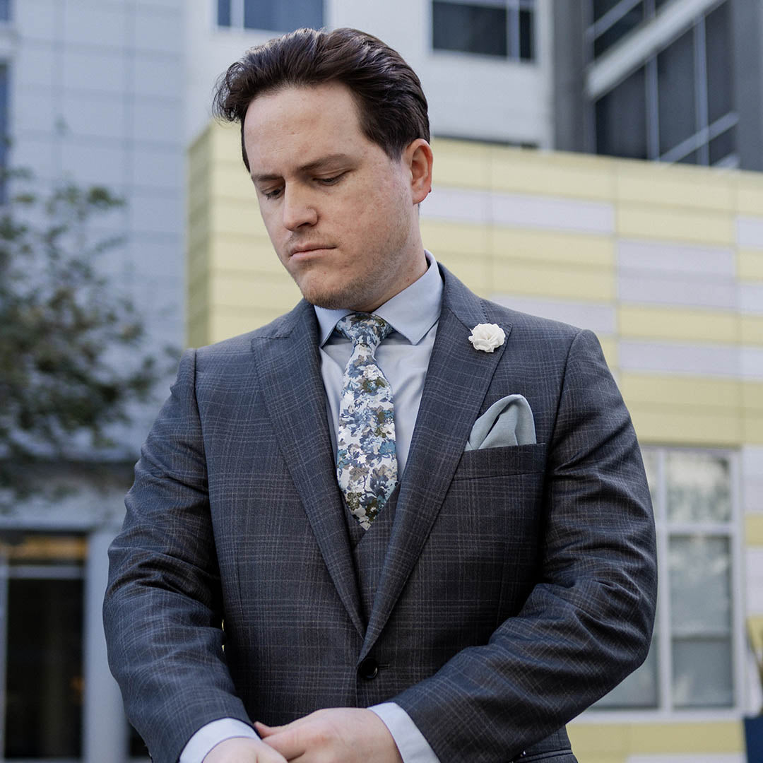 Man wearing charcoal suit with a blue shirt and blue floral tie in an urban environment