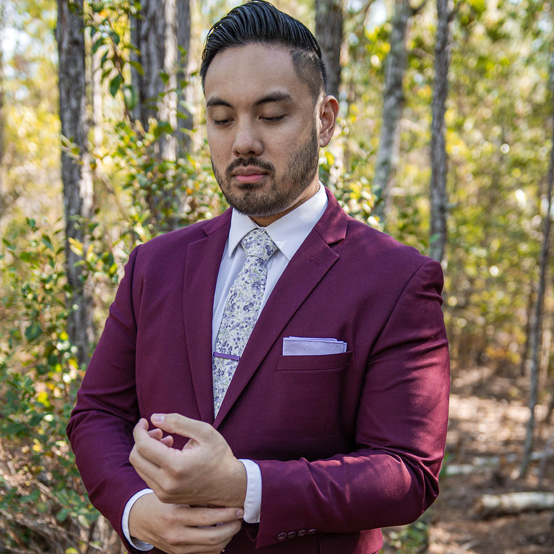 Man wearing a maroon suit in the woods with a Floral Lavender Tie