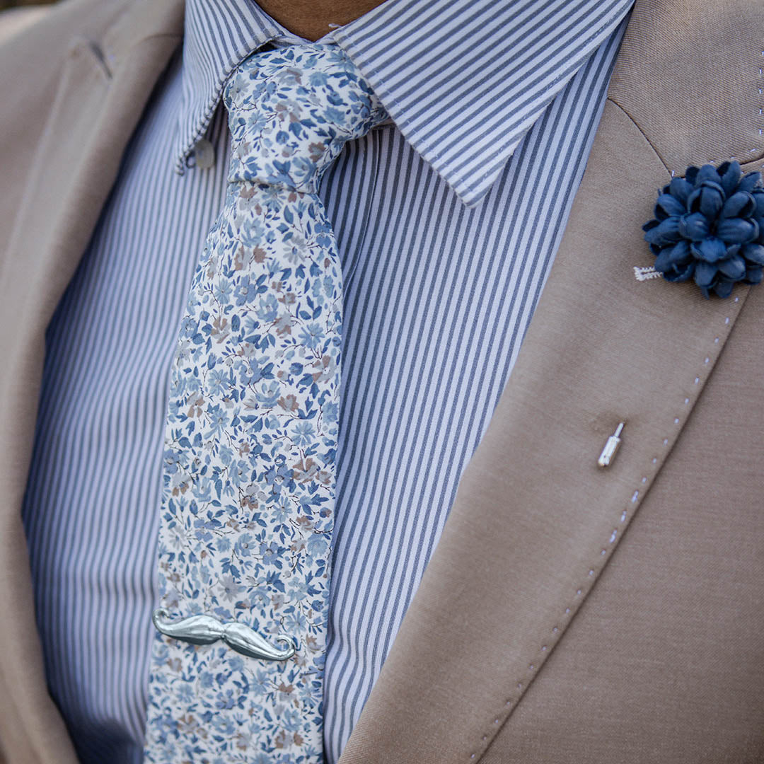 tan suit with a blue striped shirt and floral blue tie