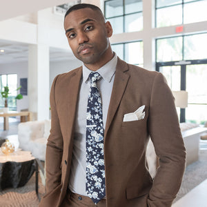 White tie bar over a floral navy tie and striped dress shirt and brown suit