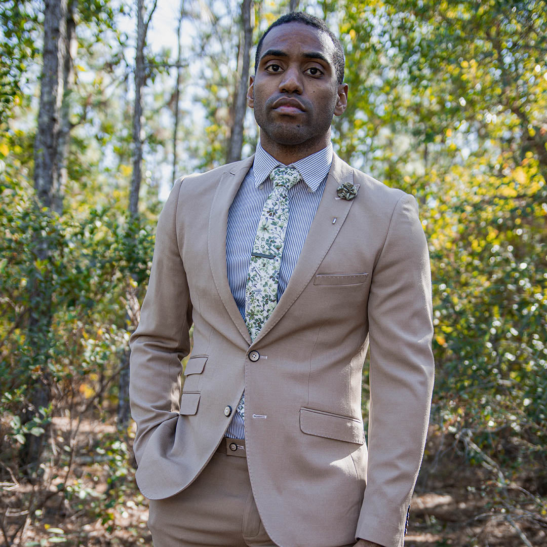 Tan suit with floral green tie on a man in a wooded area