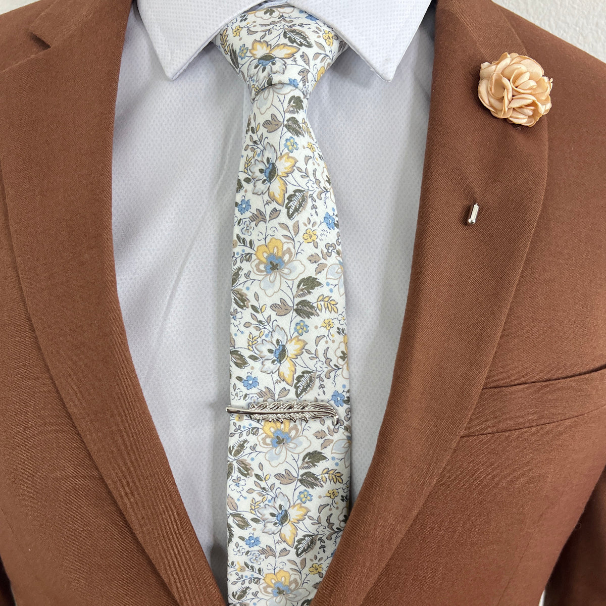 Silver Feather tie bar on a white floral tie and a brown suit
