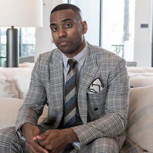 Man sitting on a couch wearing a plaid suit and the triple stripe earth metals tie set.