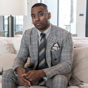 Man sitting on a couch wearing a plaid suit and the triple stripe earth metals tie set