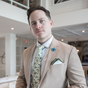 Olive border linen pocket square with a tan suit paired with a floral tie