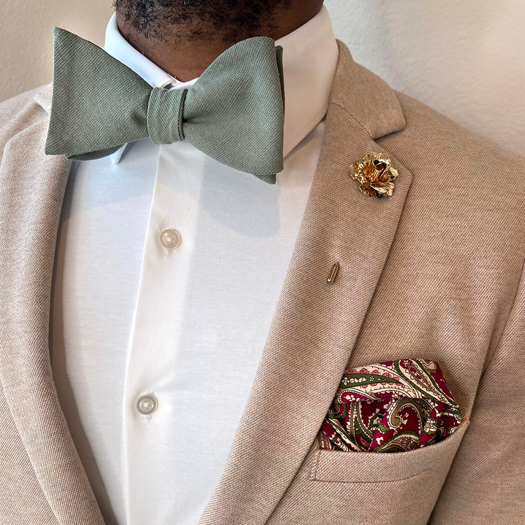 Man wearing a beige suit with a green bow tie, white shirt, and patterned pocket square.
