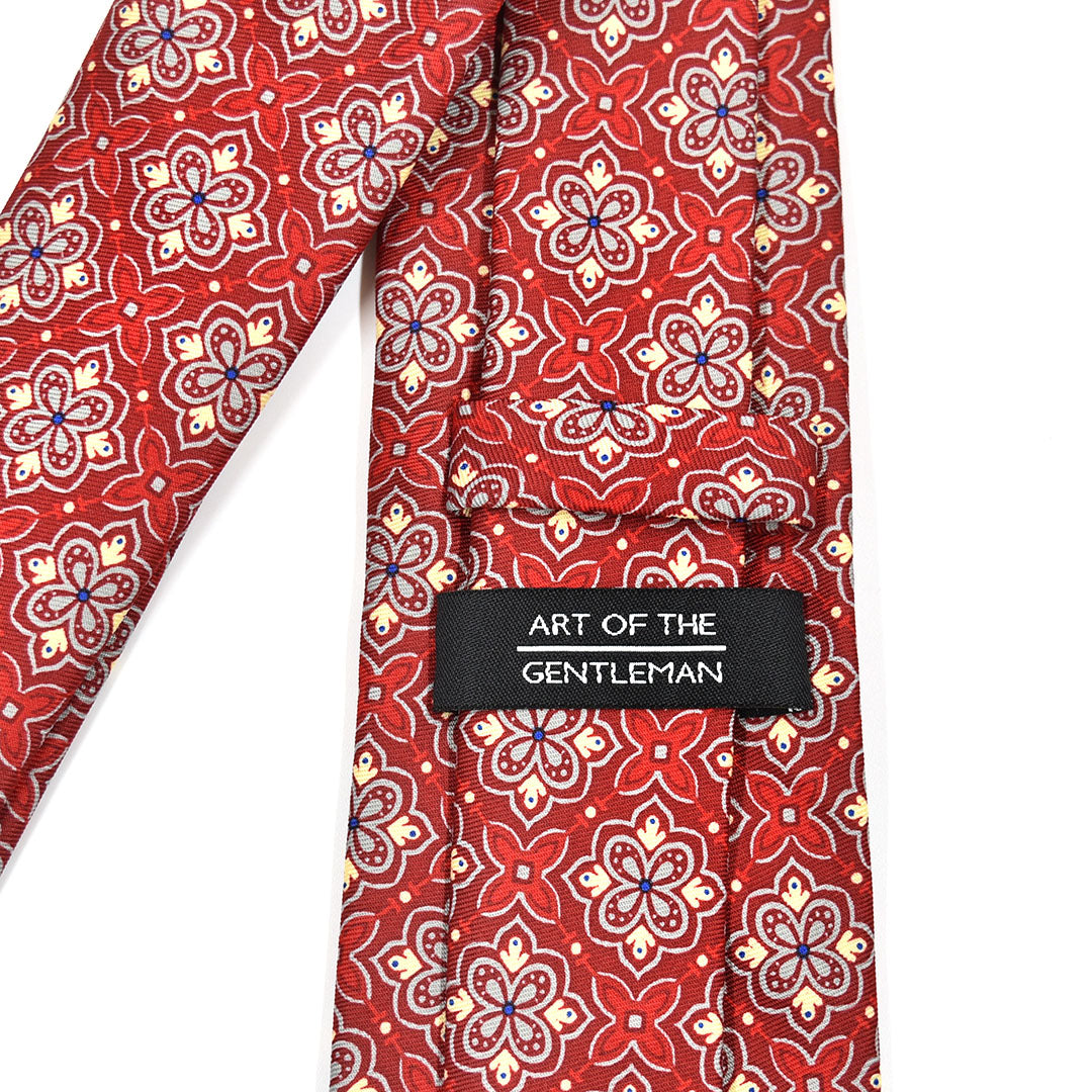 Red patterned tie with 'Art of the Gentleman' label on a white background