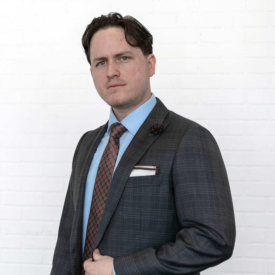 Man wearing a grey suit with a royal brown dots tie and blue shirt