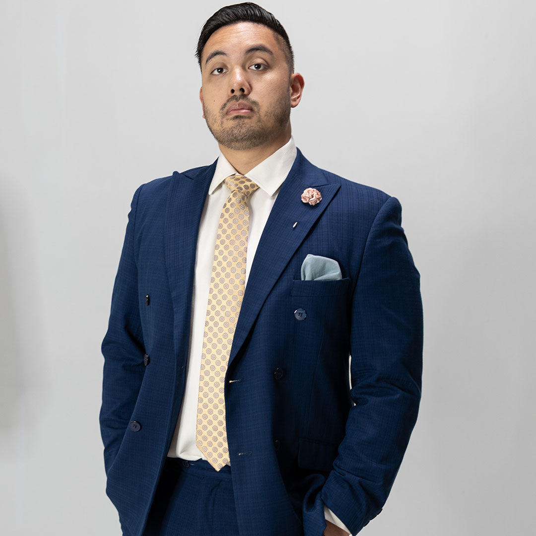 Man wearing a blue suit with a beige tie and pocket square on a plain background