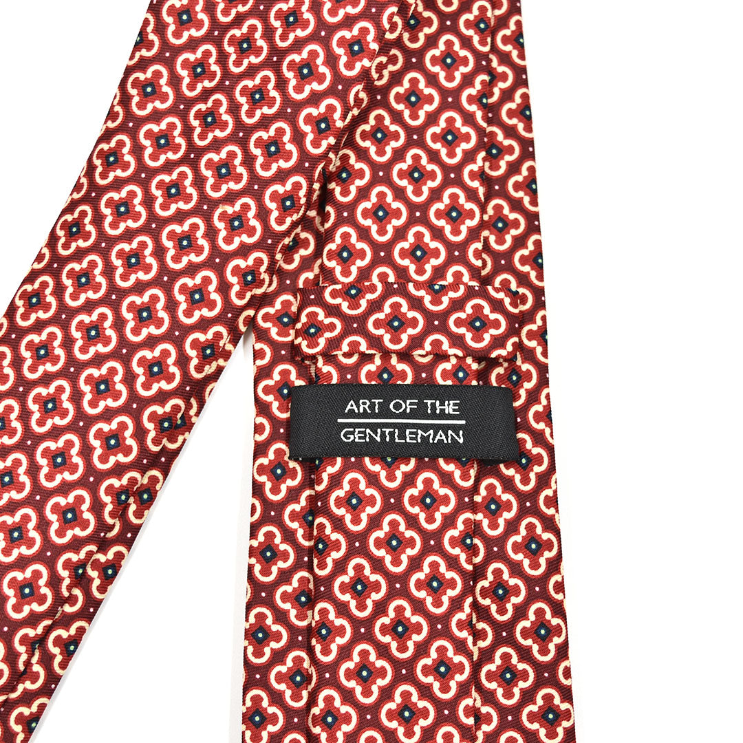 Red floral patterned tie with 'Art of the Gentleman' label on a white background