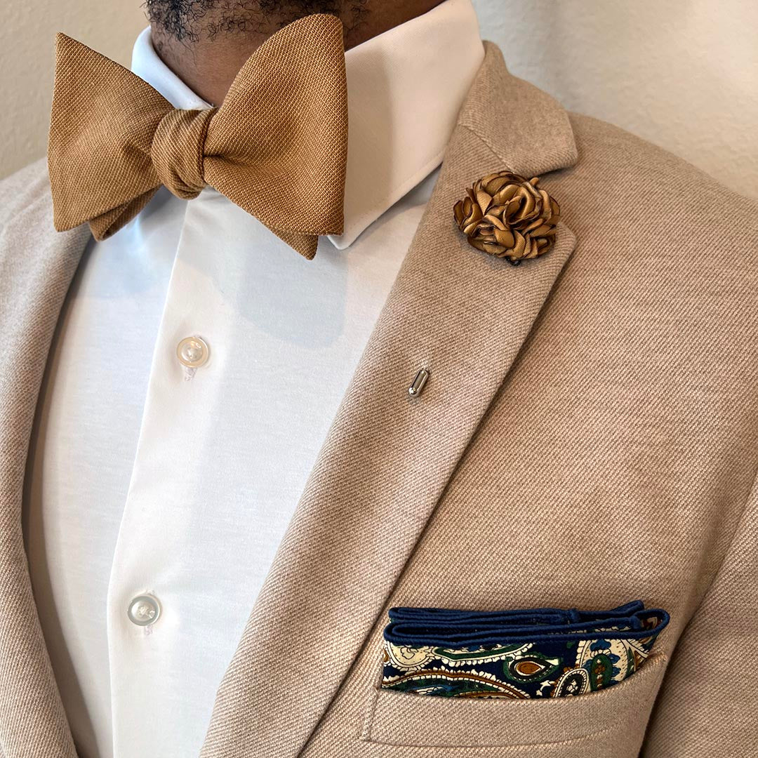 Beige suit jacket with a brown bow tie and pocket square, on a neutral background