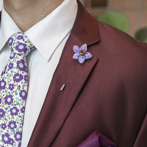 Wildflower lilac lapel pin on a burgundy suit lapel