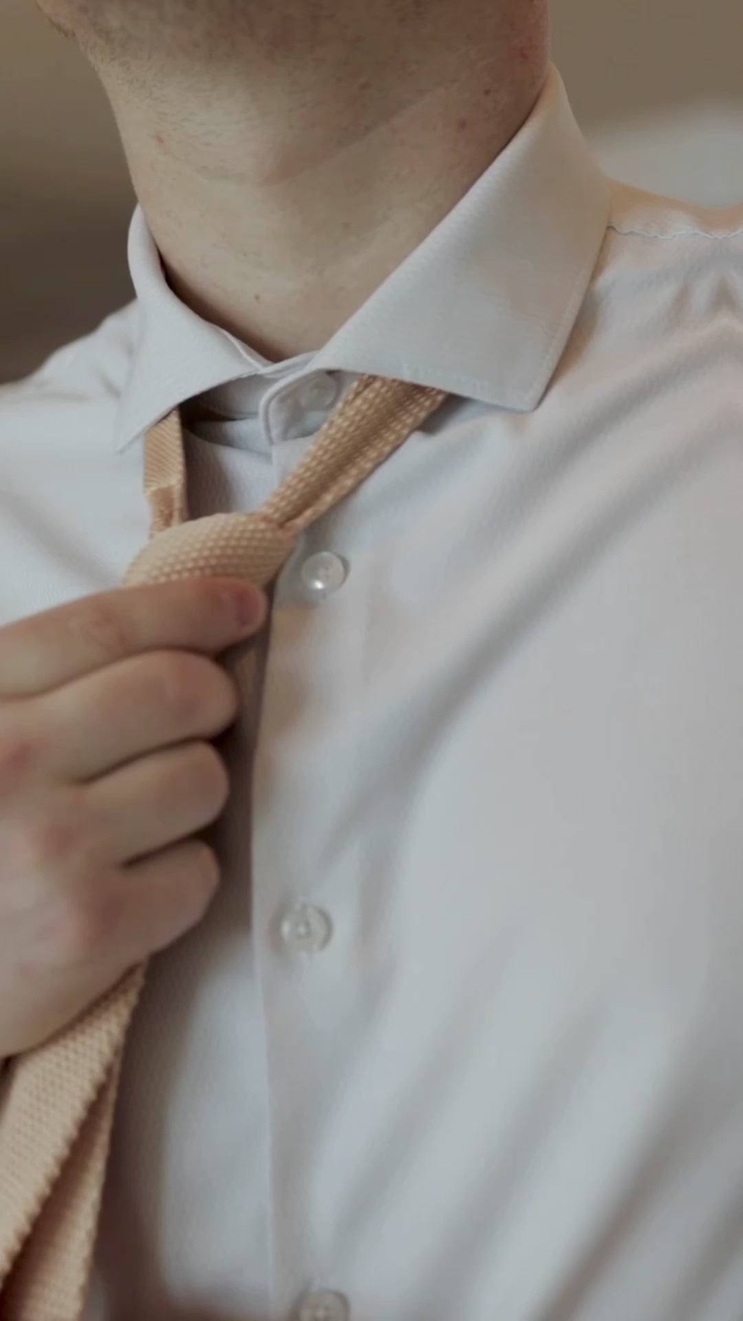 man tieing a knitted sand tie while wearing a tan suit